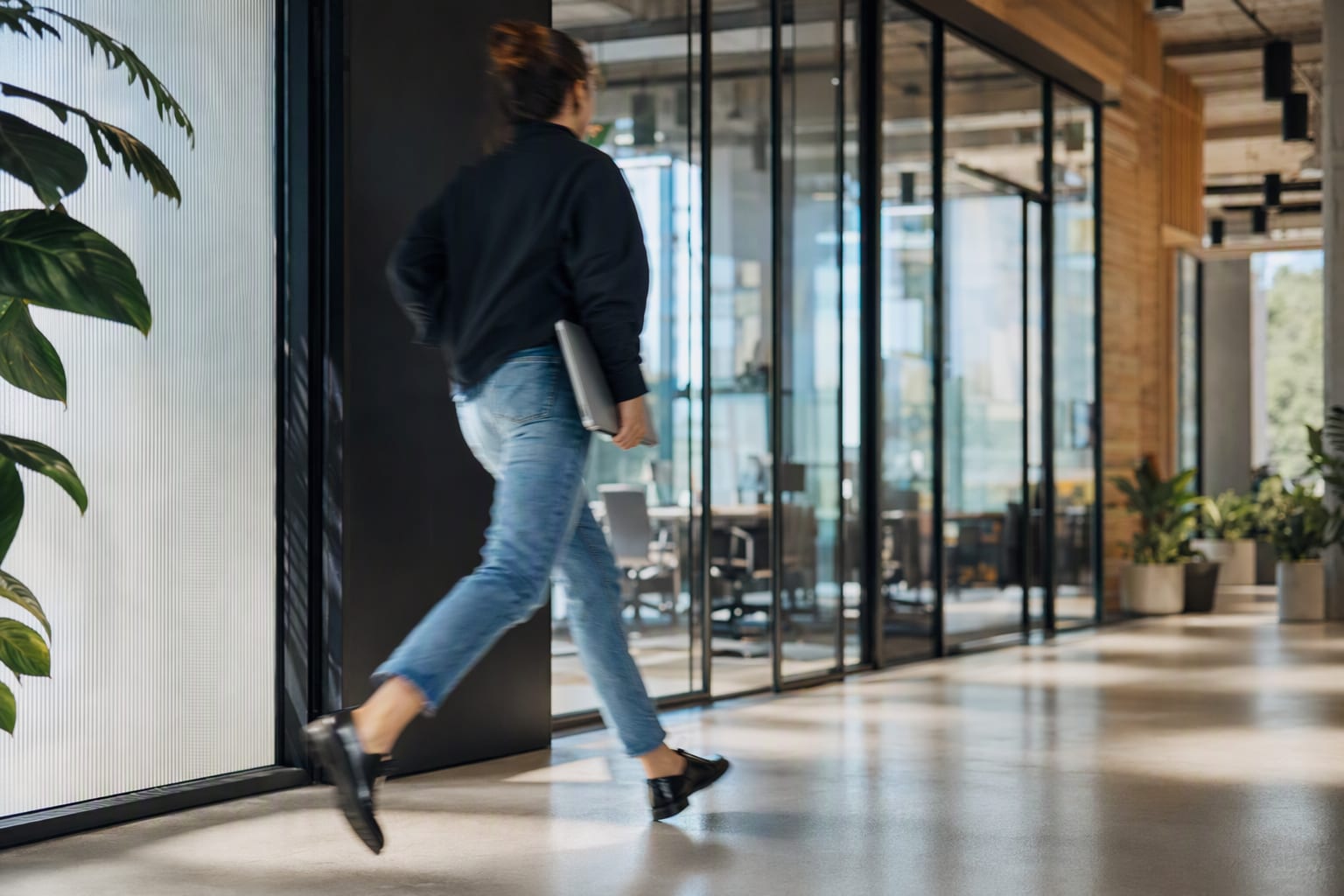 A person walking briskly through a bright office corridor with a laptop