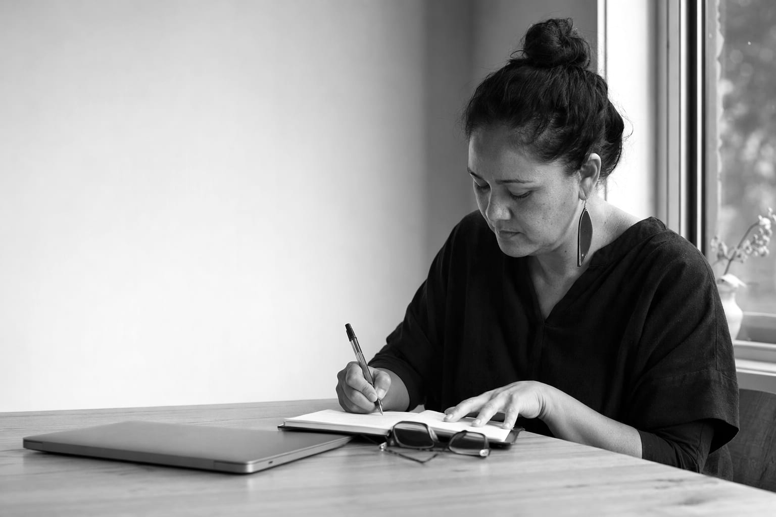 A person writing notes at a desk beside a laptop
