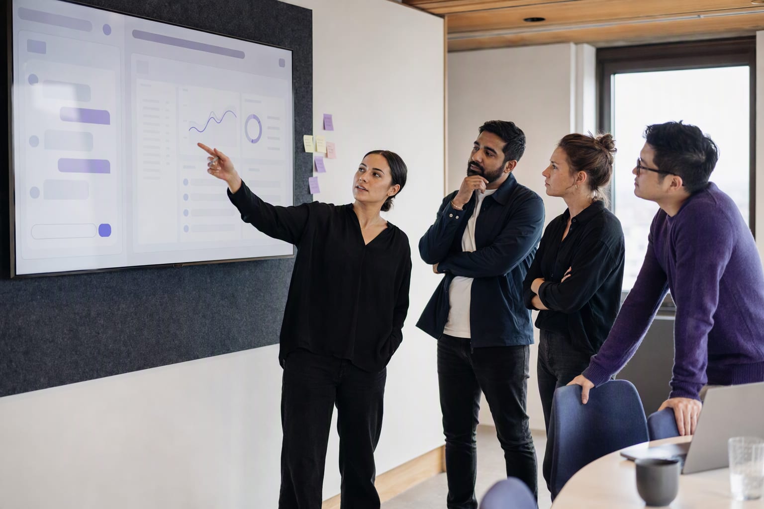 A small team in a meeting room reviewing an early AI app prototype on a large screen, one person pointing at the chat panel while the others think it through