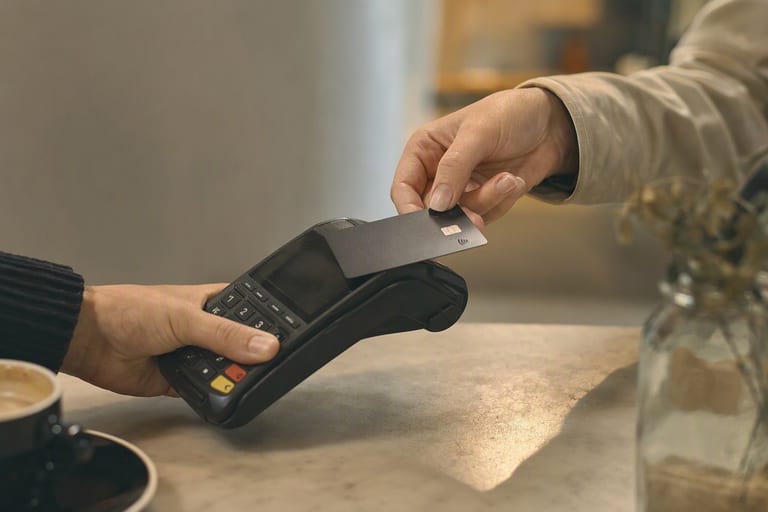 A customer taps a card on a payment terminal at a café counter